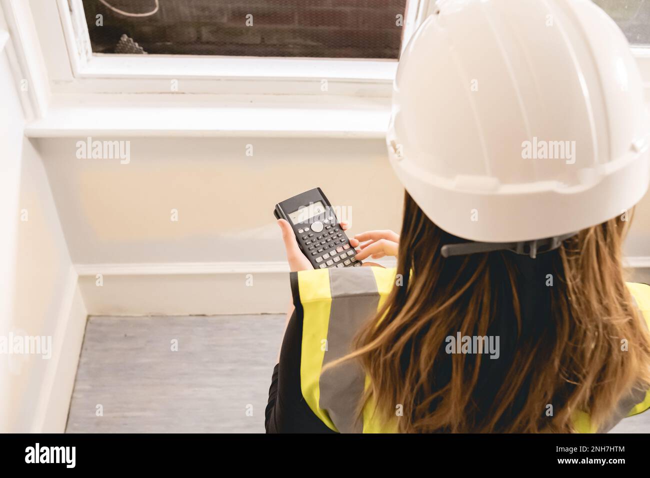 Donna di ingegnere civile irriconoscibile con capelli biondi lunghi calcolando con una calcolatrice in un cantiere, gilet giallo ad alta visibilità, p personale Foto Stock