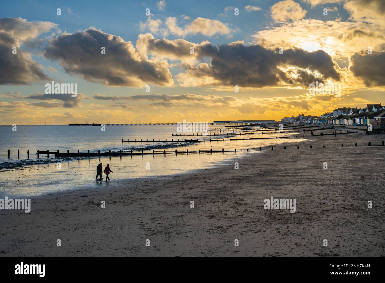 Camminatori sulla spiaggia e molo a Walton sulla Naze al tramonto Foto Stock