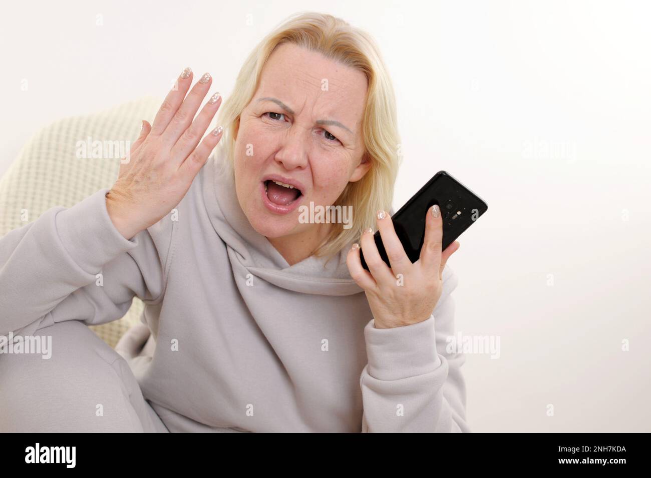 donna insoddisfatta che agita la mano mostrando al telefono che guarda la fotocamera con la bocca aperta accigliando le sopracciglia abbassando gli occhi su uno sfondo bianco cattiva consegna insoddisfazione Foto Stock