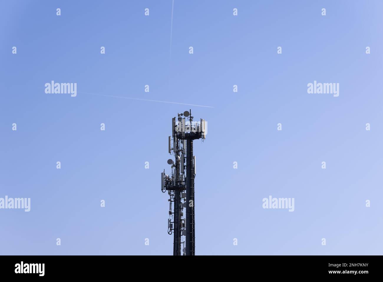 Torre per telecomunicazioni con antenne cellulari e ripetitori contro un cielo blu chiaro con due tracce di velivoli volanti Foto Stock