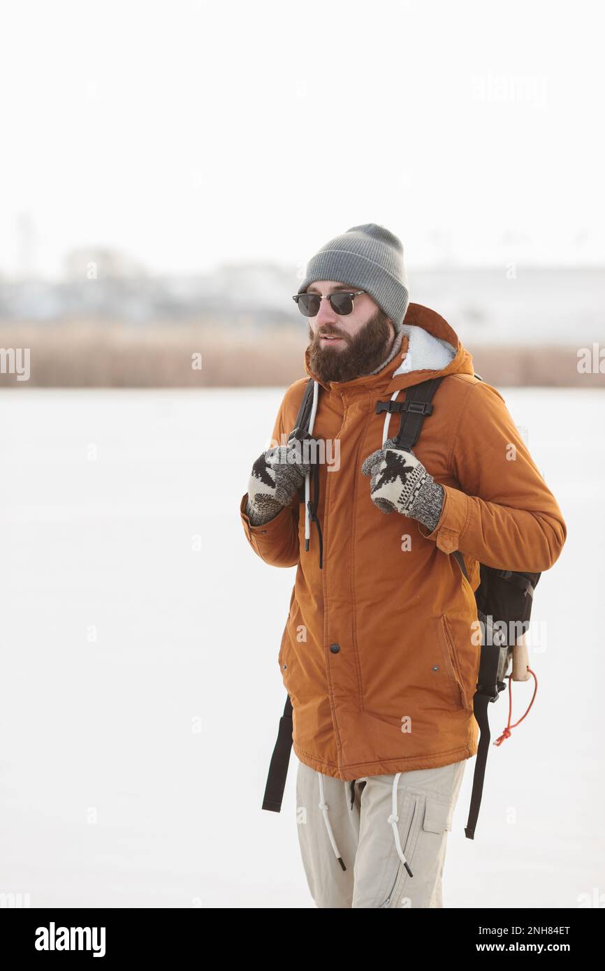 Un uomo bearded con uno zaino in abiti caldi di inverno sta camminando su un lago ghiacciato in inverno. Il concetto di trekking e di stile di vita attivo. Foto Stock