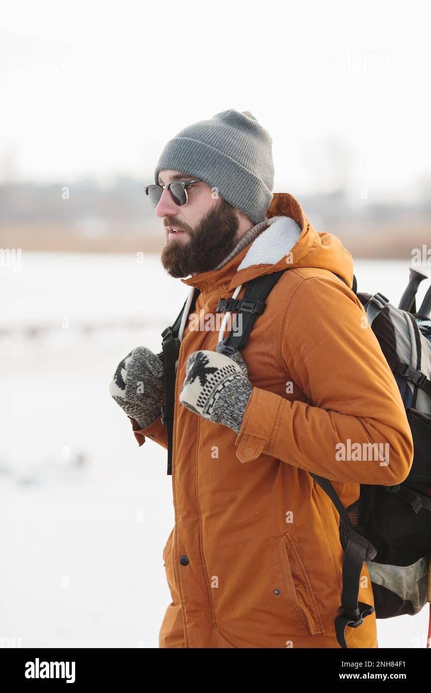 Un uomo bearded con uno zaino in abiti caldi di inverno sta camminando su un lago ghiacciato in inverno. Il concetto di trekking e di stile di vita attivo. Foto Stock