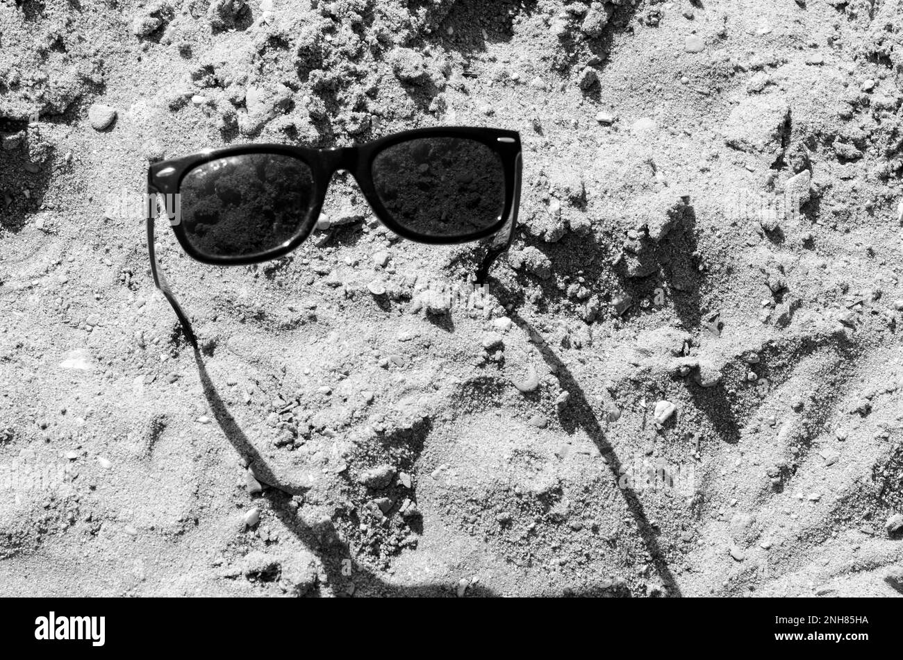 Occhiali da sole, incastrati nella sabbia, gettano un'ombra. Foto Stock