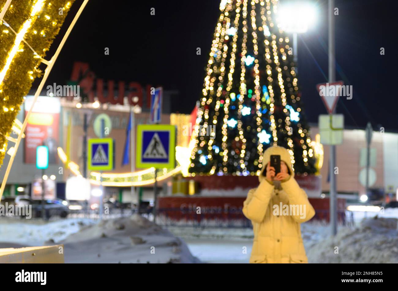 Silhouette di una ragazza sotto l'arco luminoso foto sul telefono cellulare del negozio 'Auchan' e decorazioni per le vacanze albero di Natale in inverno Foto Stock