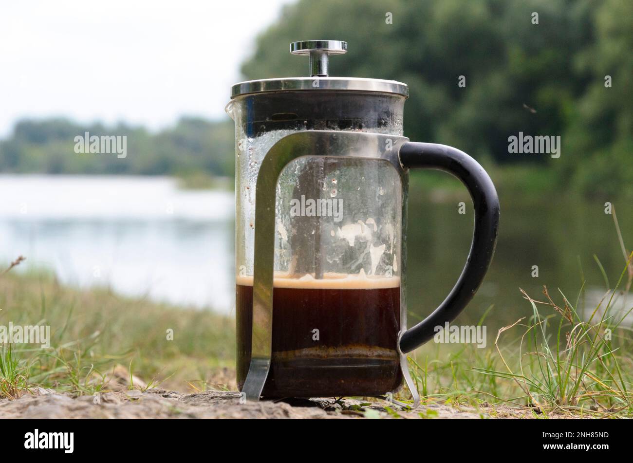 Caffè preparato in una pressa francese sulle pietre nel fiume nella foresta vicino all'erba. Foto Stock