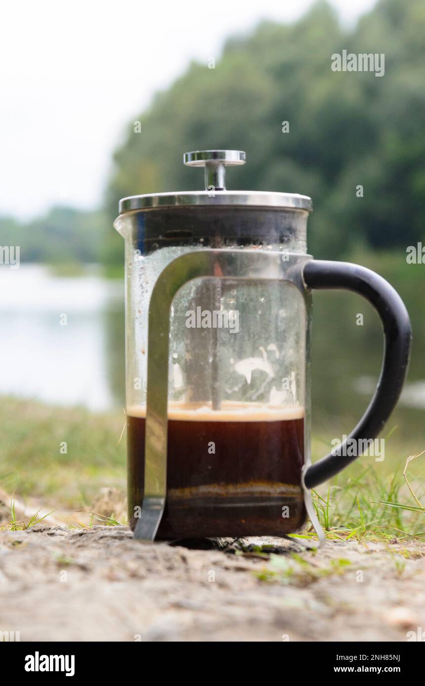 Caffè preparato in una pressa francese sulle pietre nel fiume nella foresta vicino all'erba. Foto Stock