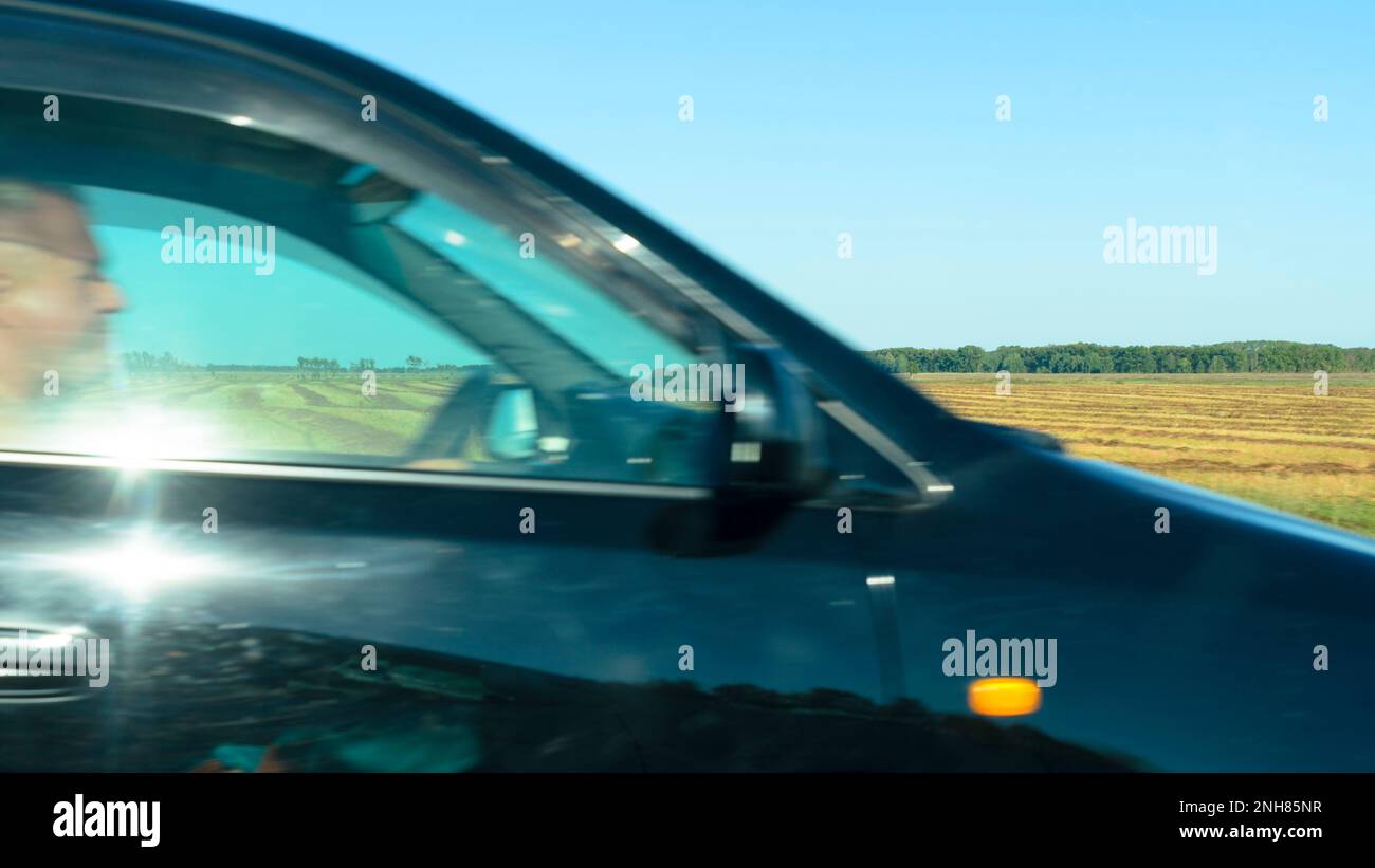 Profilo sfocato del viso del conducente, gli uomini al volante muovendosi rapidamente sulla strada la vettura blu con il riflesso del sole Foto Stock