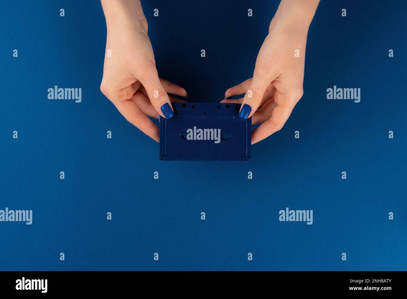 Mini videocassetta in mani femminili su sfondo blu classico Foto Stock