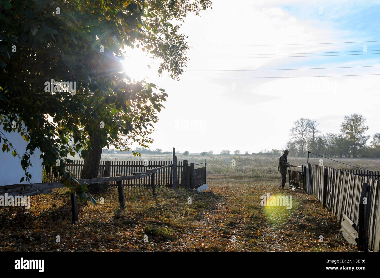 La silhouette dei vecchi nei raggi luminosi del sole di tramonto dietro gli alberi vicino alla casa colonica, apre il cancello alla recinzione per andare Foto Stock