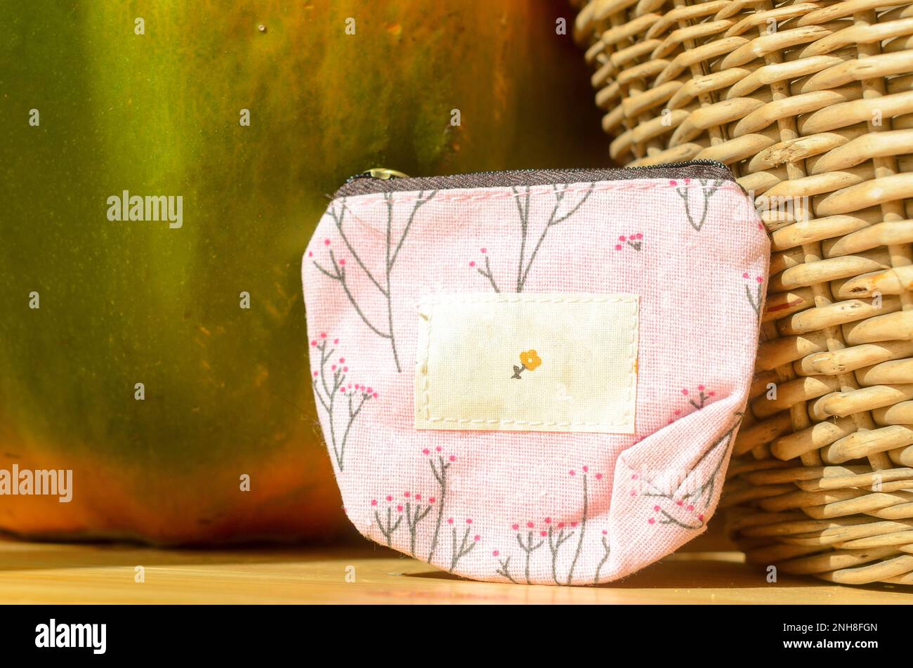 Un piccolo portamonete, una pochette con disegni a colori, si trova su un tavolo di legno vicino al cesto, fermo vita. Foto Stock