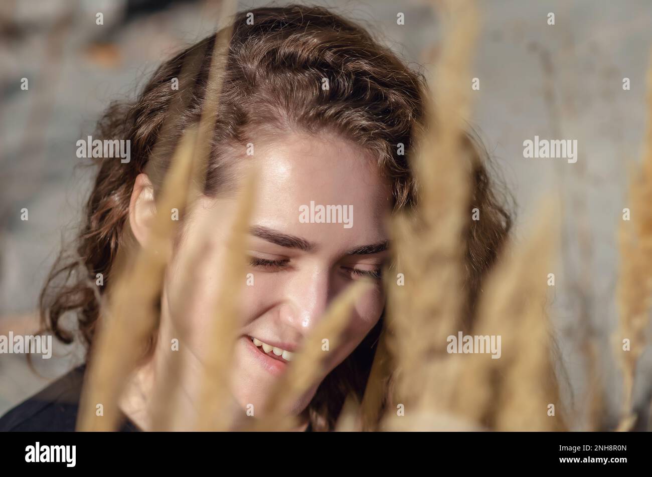 Ridendo il volto della donna in erba campo, fiori secchi. Capelli ricci. Autunno Foto Stock