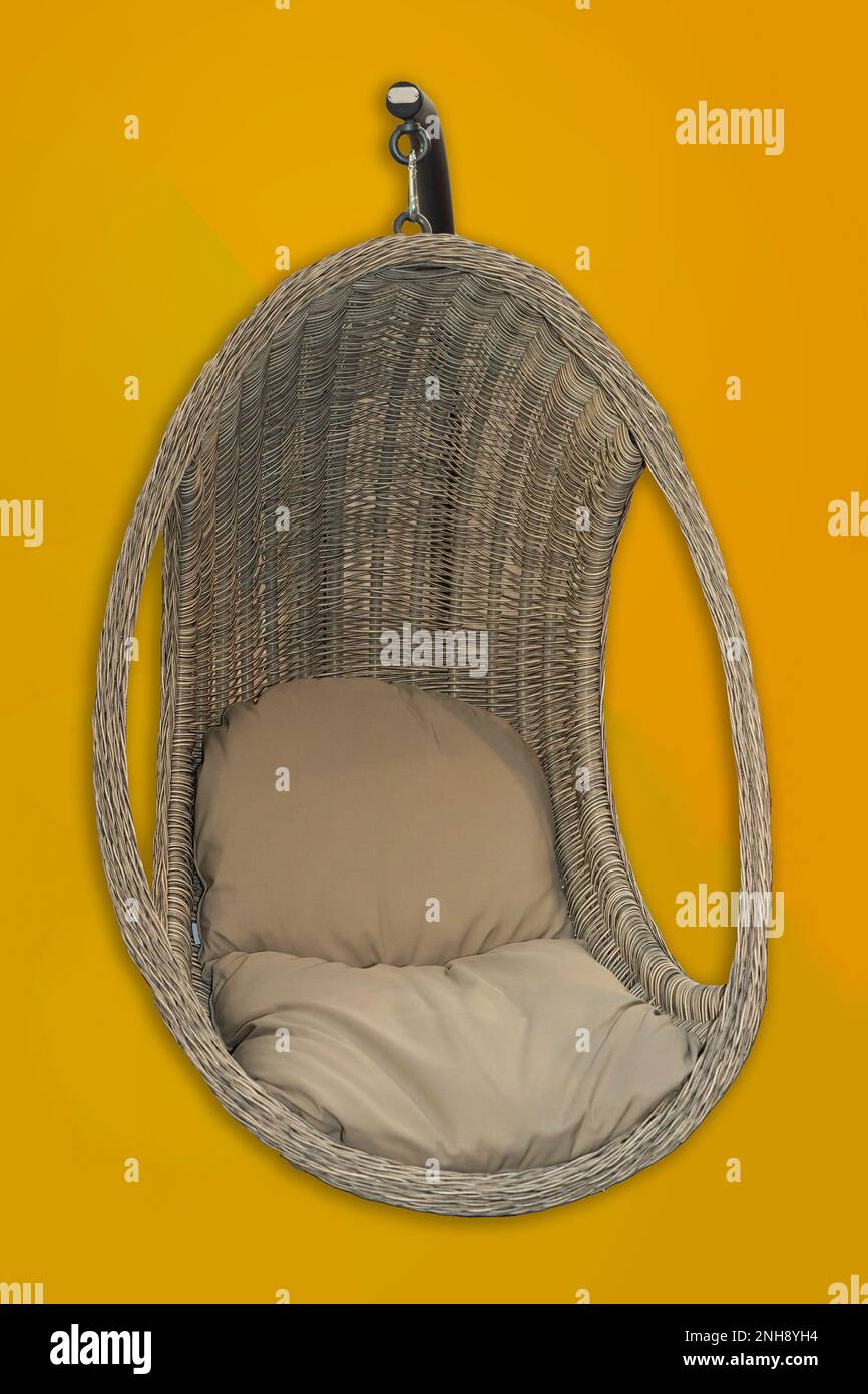 Arredamento con sedia sospesa in rattan, con un piedistallo e un comodo cuscino isolato sul giallo Foto Stock