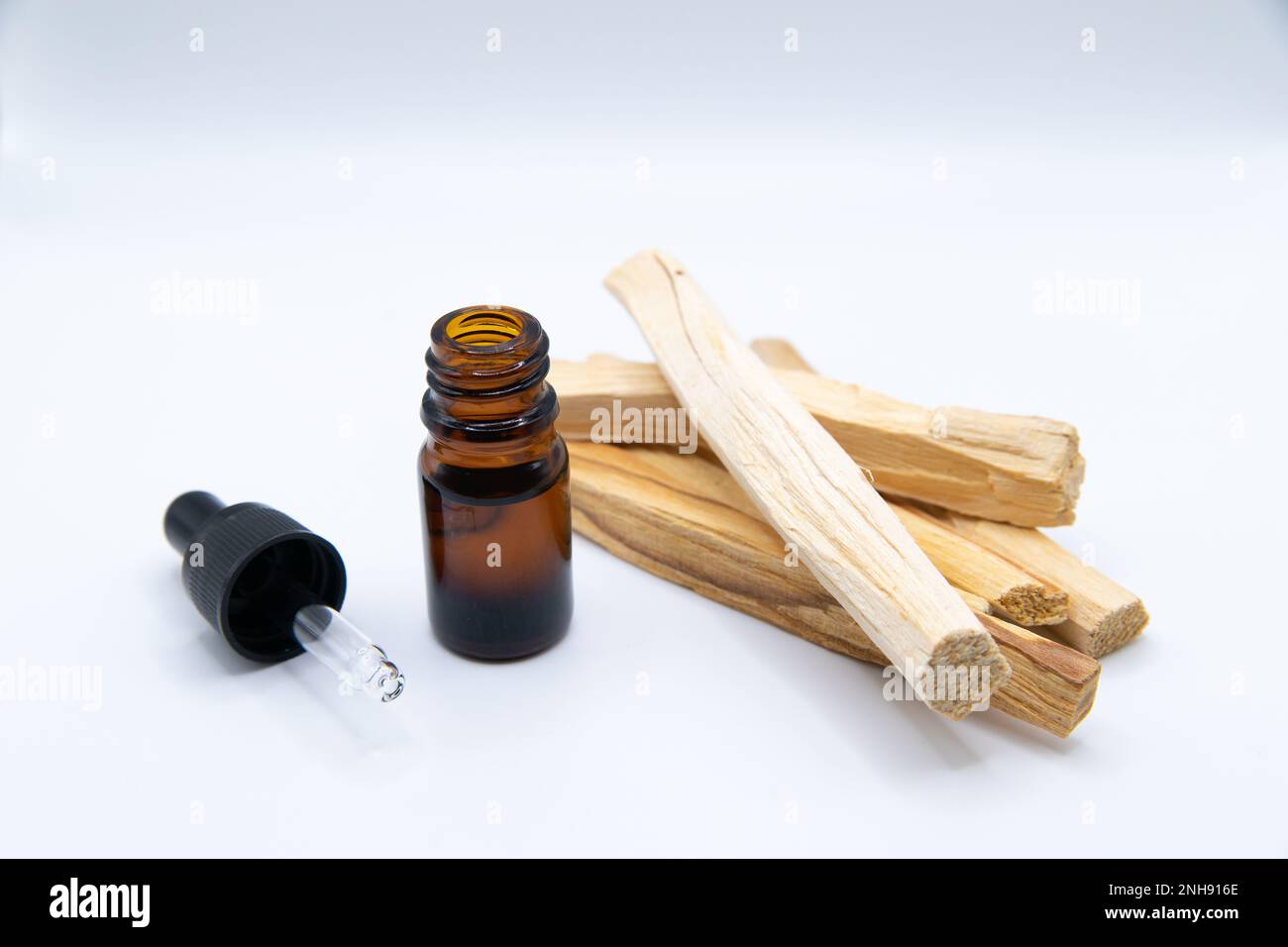 Palo Santo (bastone Santo) estratto di olio essenziale Essense in una bottiglia con bastoncini di Palo Santo accanto ad esso. Primo piano isolato su sfondo bianco. Foto Stock