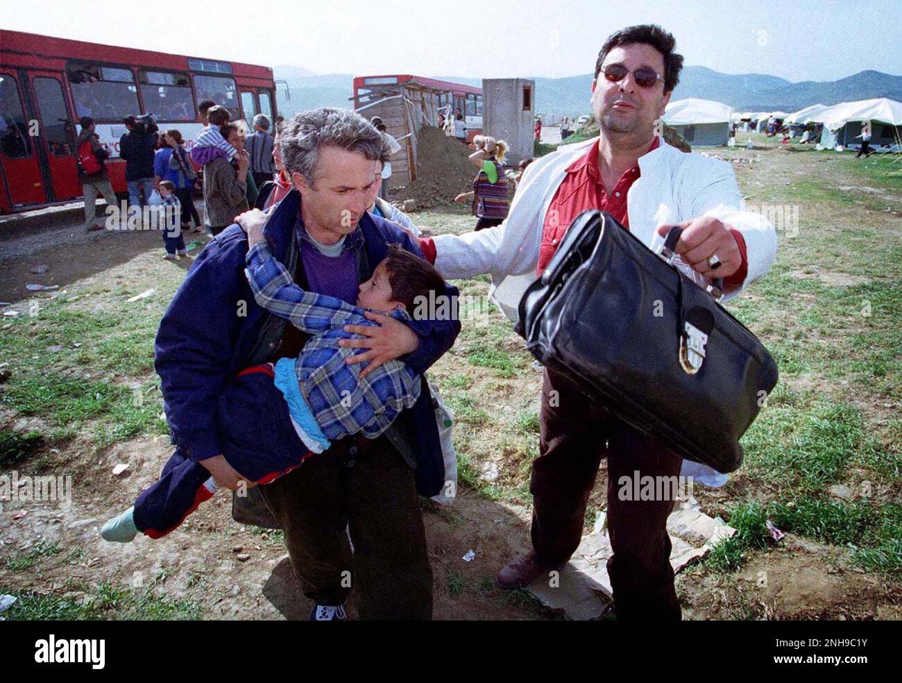 L'uomo corre con il bambino per cercare aiuto medico con il medico. Uomo e bambino erano fuggiti dal Kosovo a causa della pulizia etnica ed erano arrivati nella Macedonia settentrionale via autobus dalla traversata del confine. Campo profughi di Brazda in Macedonia Aprile 1999. Il campo è stato gestito dalla NATO, ma è passato all'UNHCR. Macedonia. Figura garyrobertsphotography.com Foto Stock