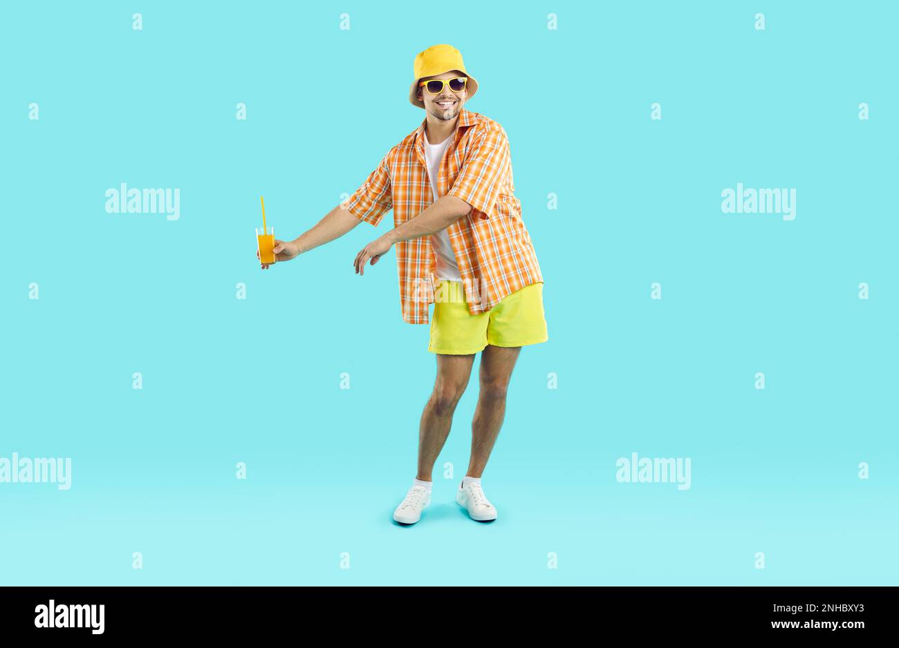 Felice giovane uomo caucasico turista esegue danza con un bicchiere di succo in mano, stand in studio Foto Stock