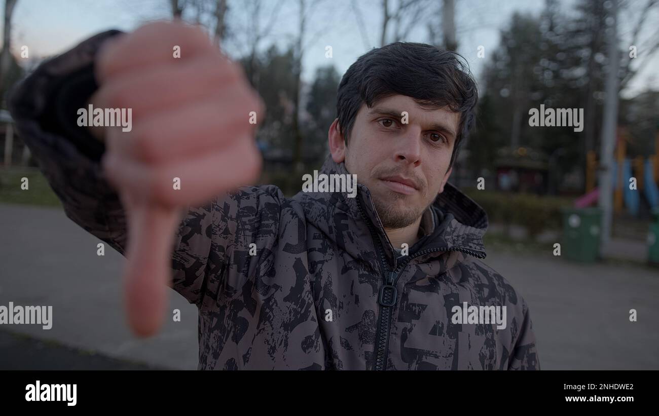 Serious Young Man non ama qualcosa, mostrando i Thumb fino alla fotocamera all'aperto Foto Stock