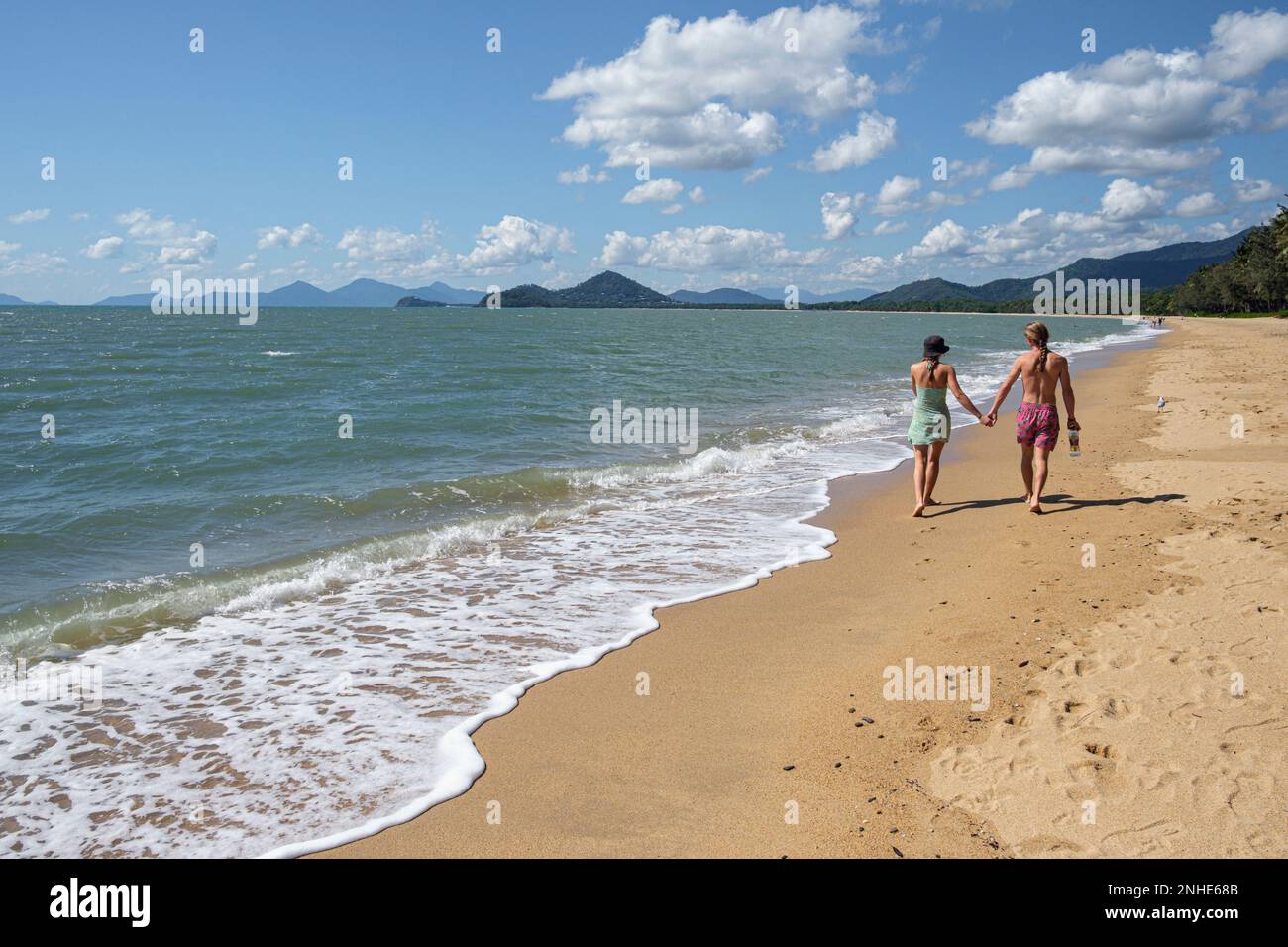 Una giovane coppia cammina di pari passo lungo la spiaggia di Palm Cove, Queensland, Australia Foto Stock