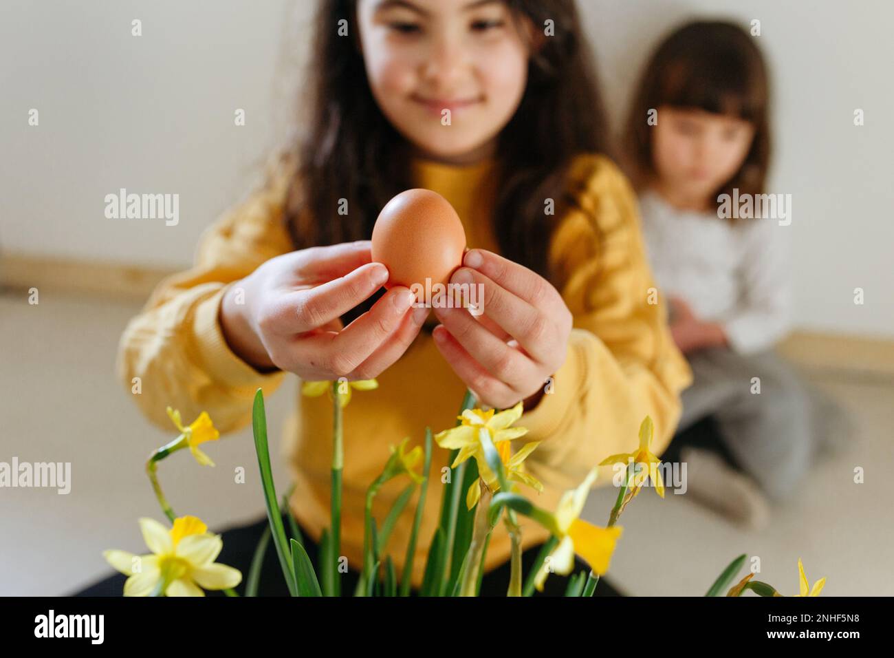 Ragazza seduta in cima gialla tenendo l'uovo di Pasqua in mano mentre la ragazza più piccola si siede dietro Foto Stock