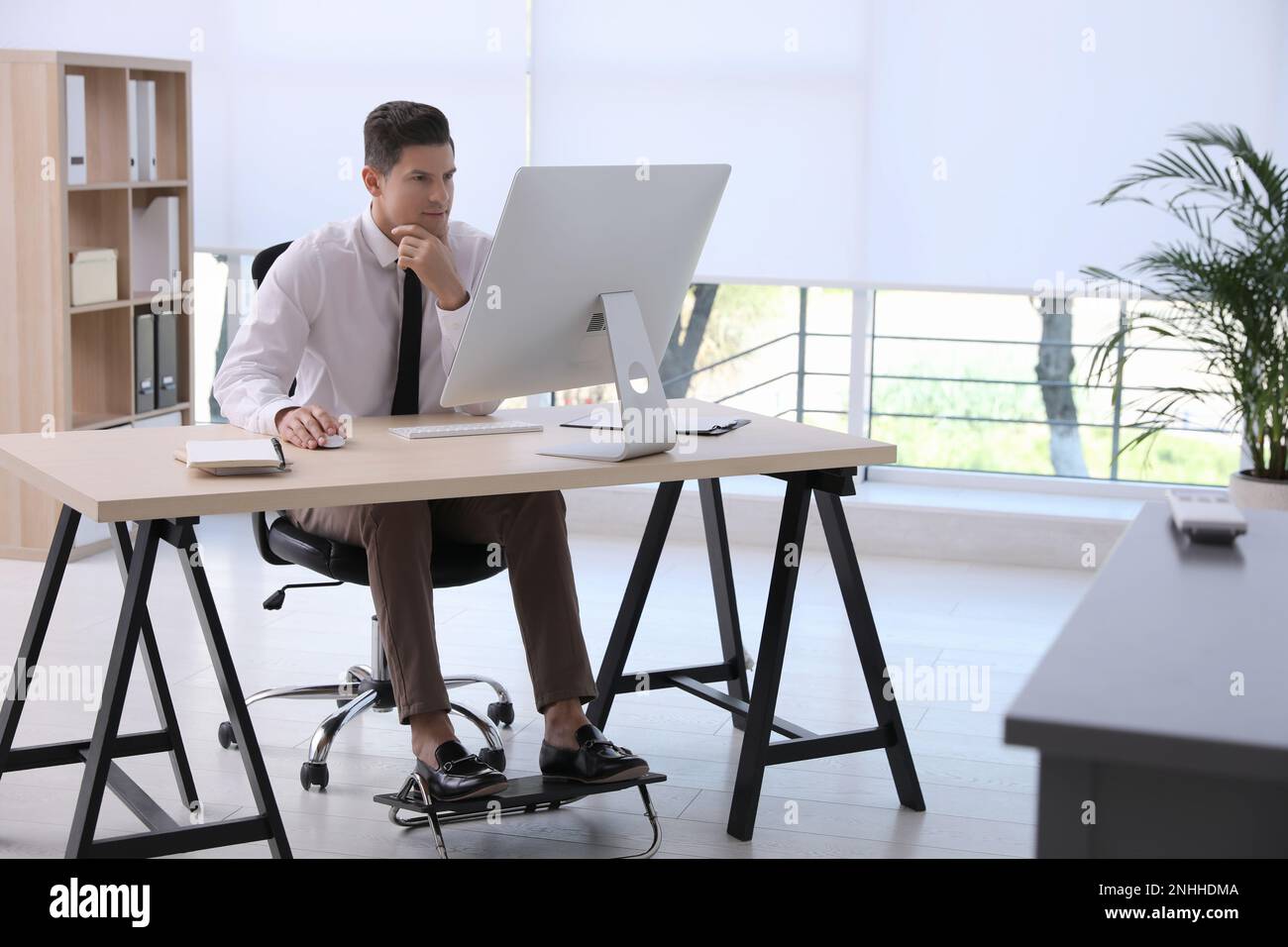 Uomo che usa il poggiapiedi mentre lavora al computer in ufficio Foto Stock