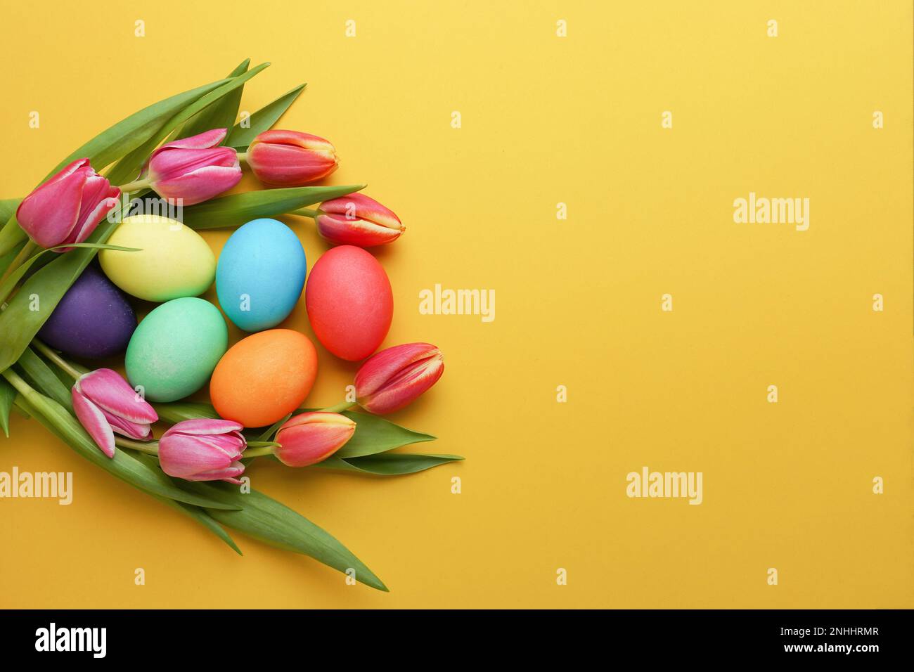 Fiori di tulipano freschi e colorati e uova di pasqua su sfondo giallo. Vista dall'alto con spazio di copia. Auguri di buona pasqua. Foto Stock
