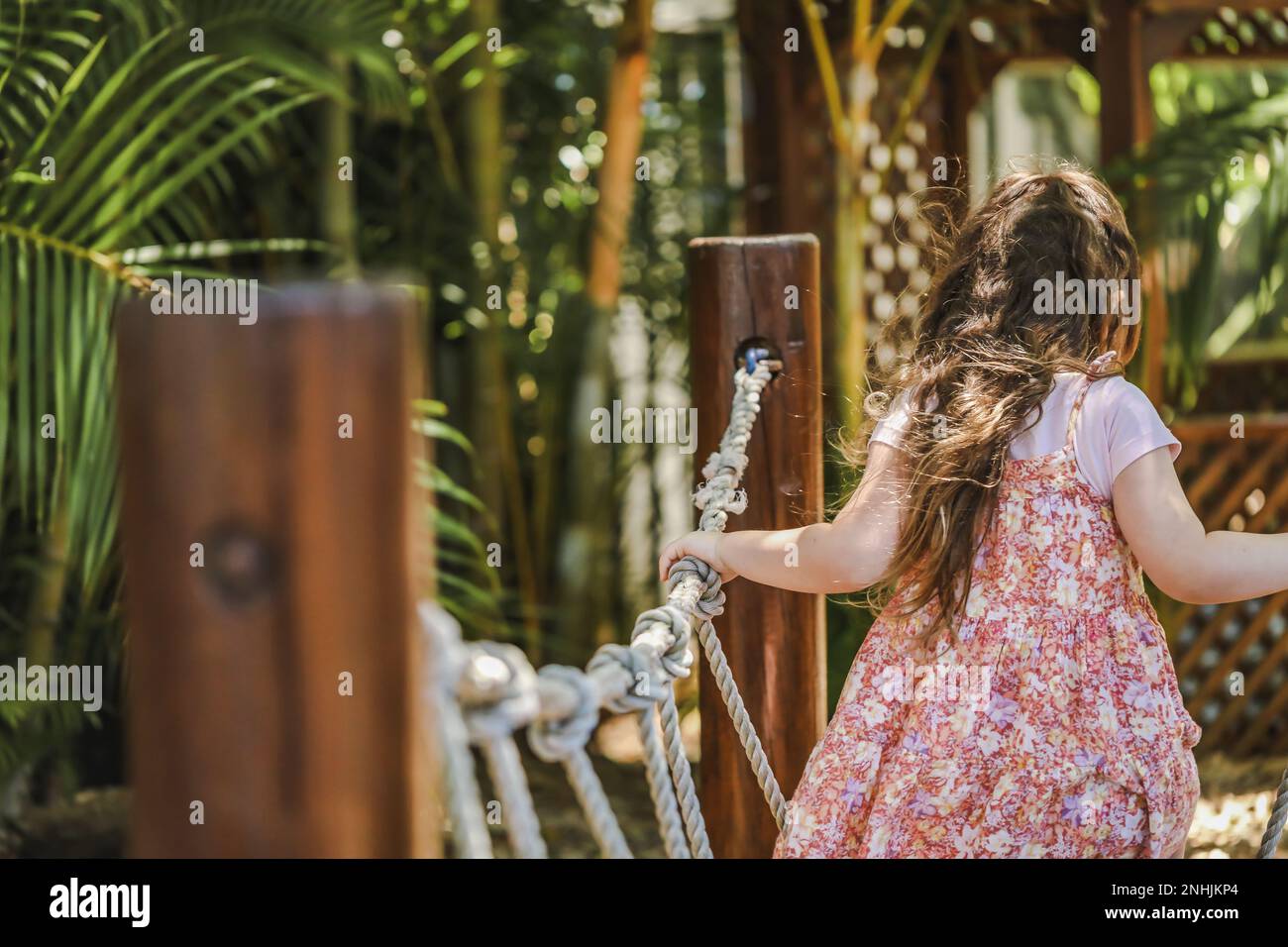 Bambino di prescolare che gioca sull'oscillazione della corda. Bellissimo giardino tropicale per bambini. Foto Stock