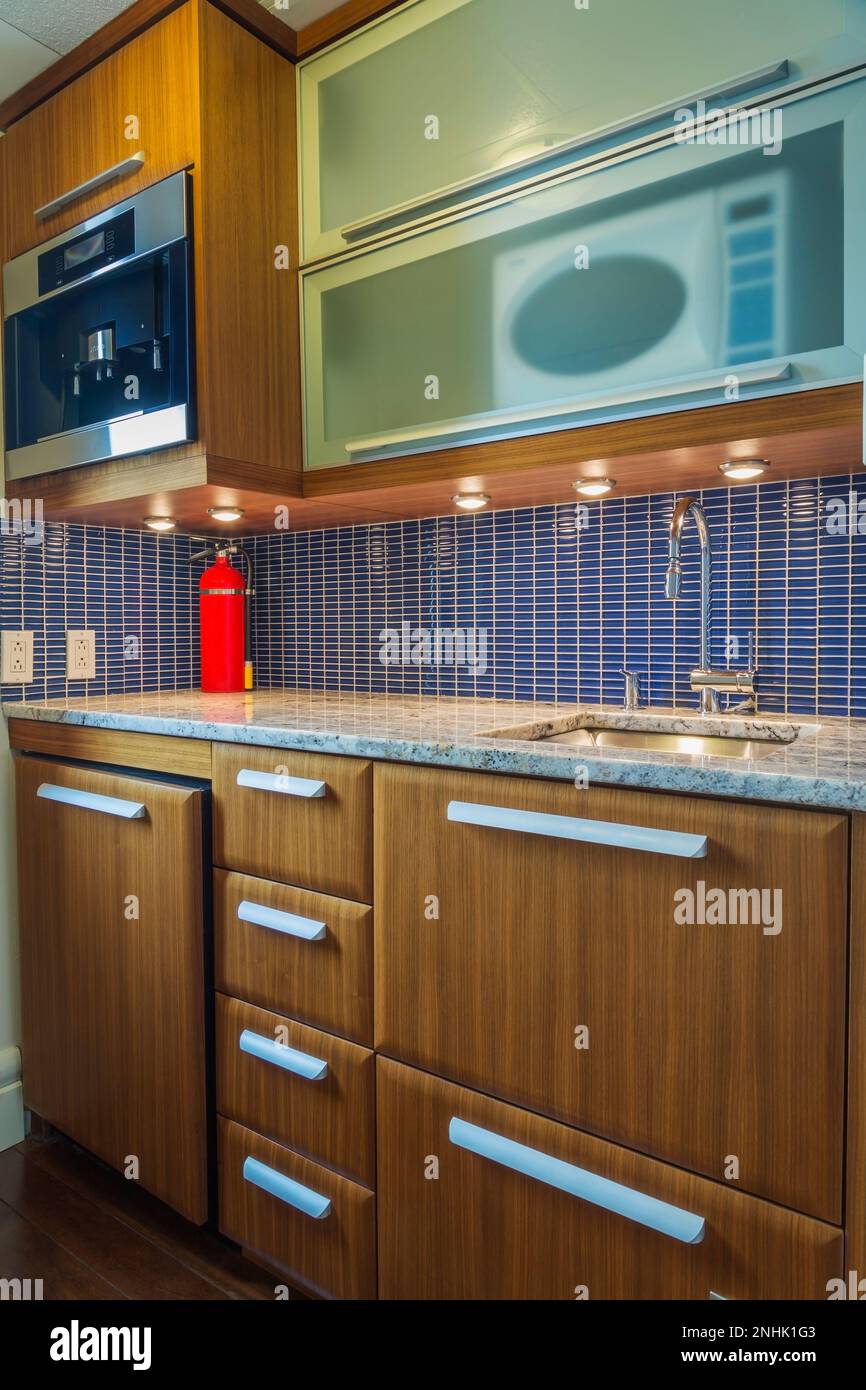 Piccolo cucinotto con ripiani in granito sfumato e sfondo in ceramica blu all'interno di un moderno e lussuoso condominio attico a più piani. Foto Stock