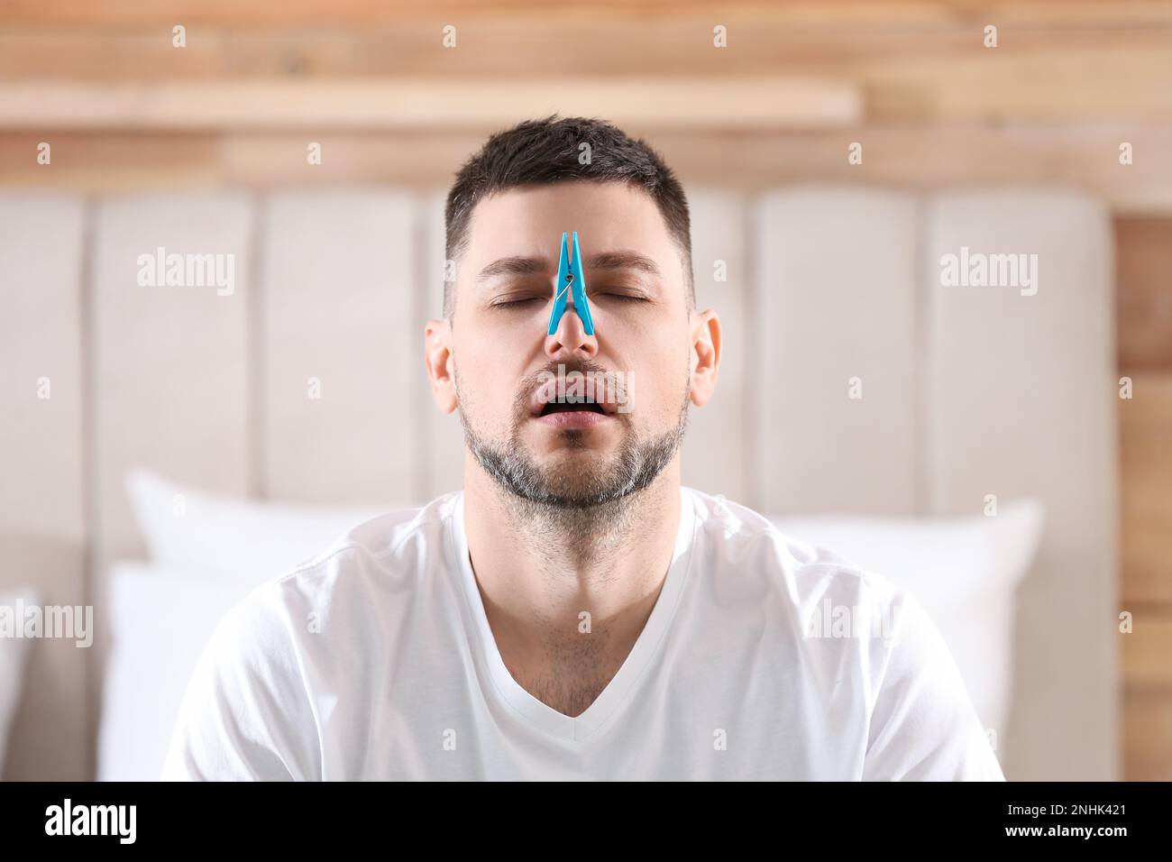 Uomo con clothespin che soffre di naso che cola in camera da letto Foto Stock