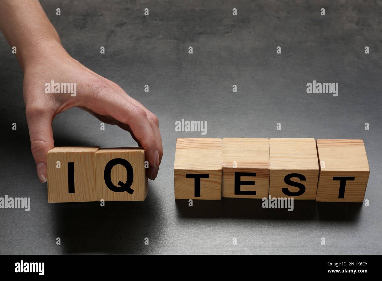 Donna che prende cubi con testo IQ Test su sfondo grigio, primo piano Foto Stock