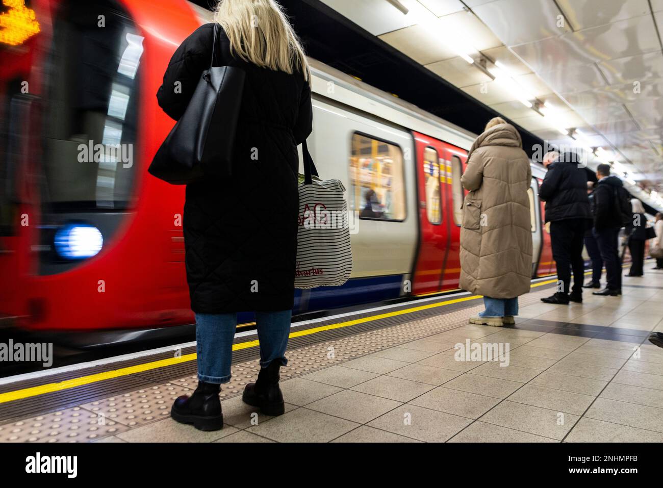 I passeggeri che aspettano sulla piattaforma della metropolitana di Londra con il treno della metropolitana che arriva in stazione. Stazione di Westminster. Femmina con borse Foto Stock