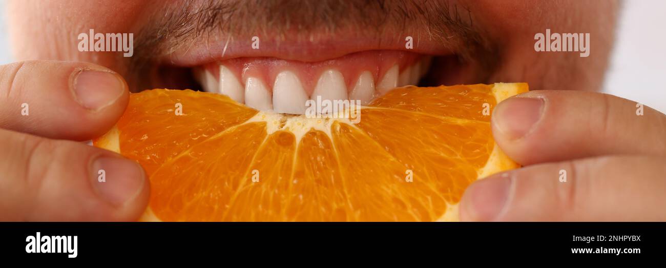 L'uomo sorridente bearded tiene e morde la frutta dell'arancia Foto Stock