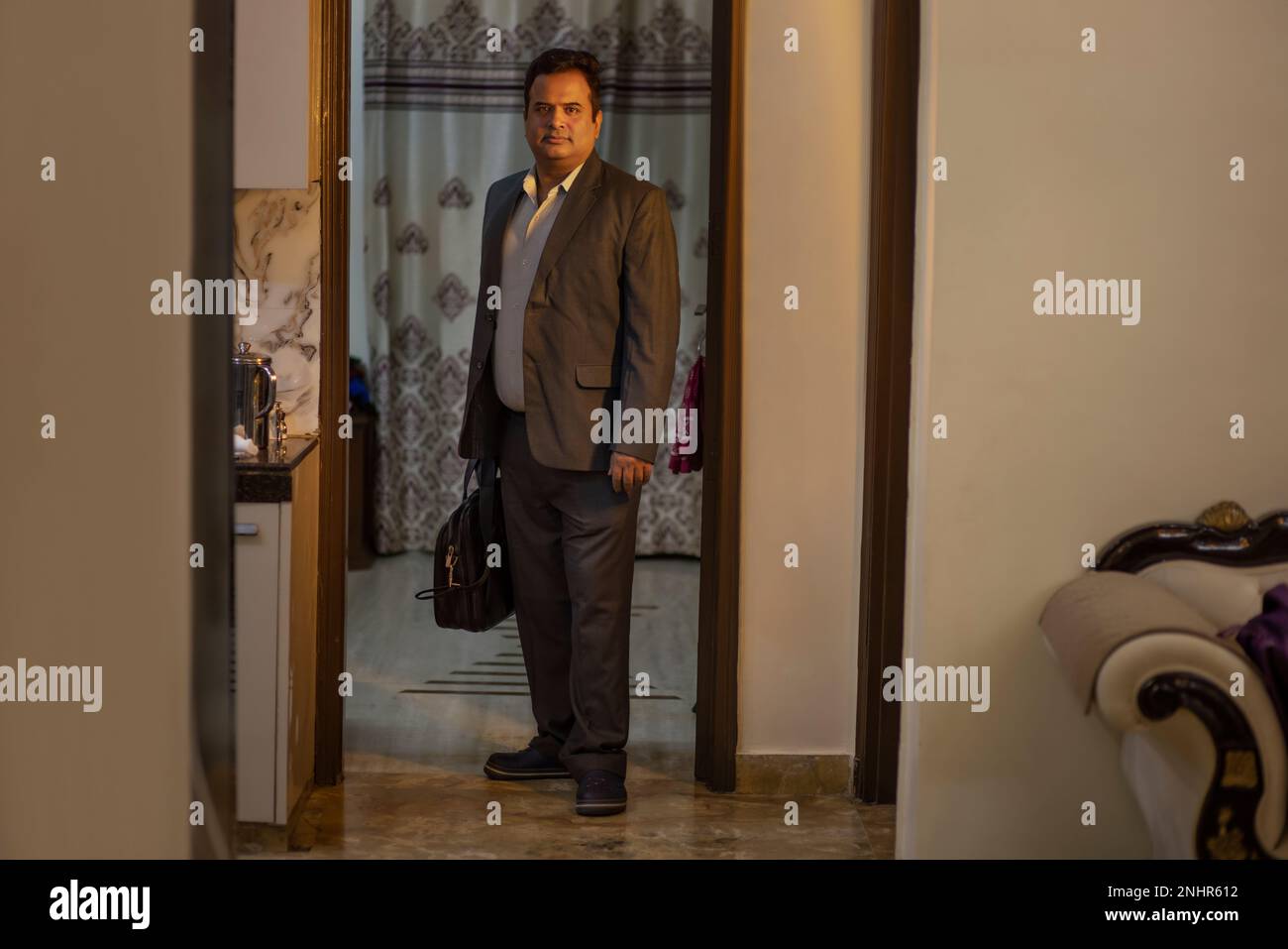 Uomo in abiti formali in piedi con borsa da ufficio a casa Foto Stock
