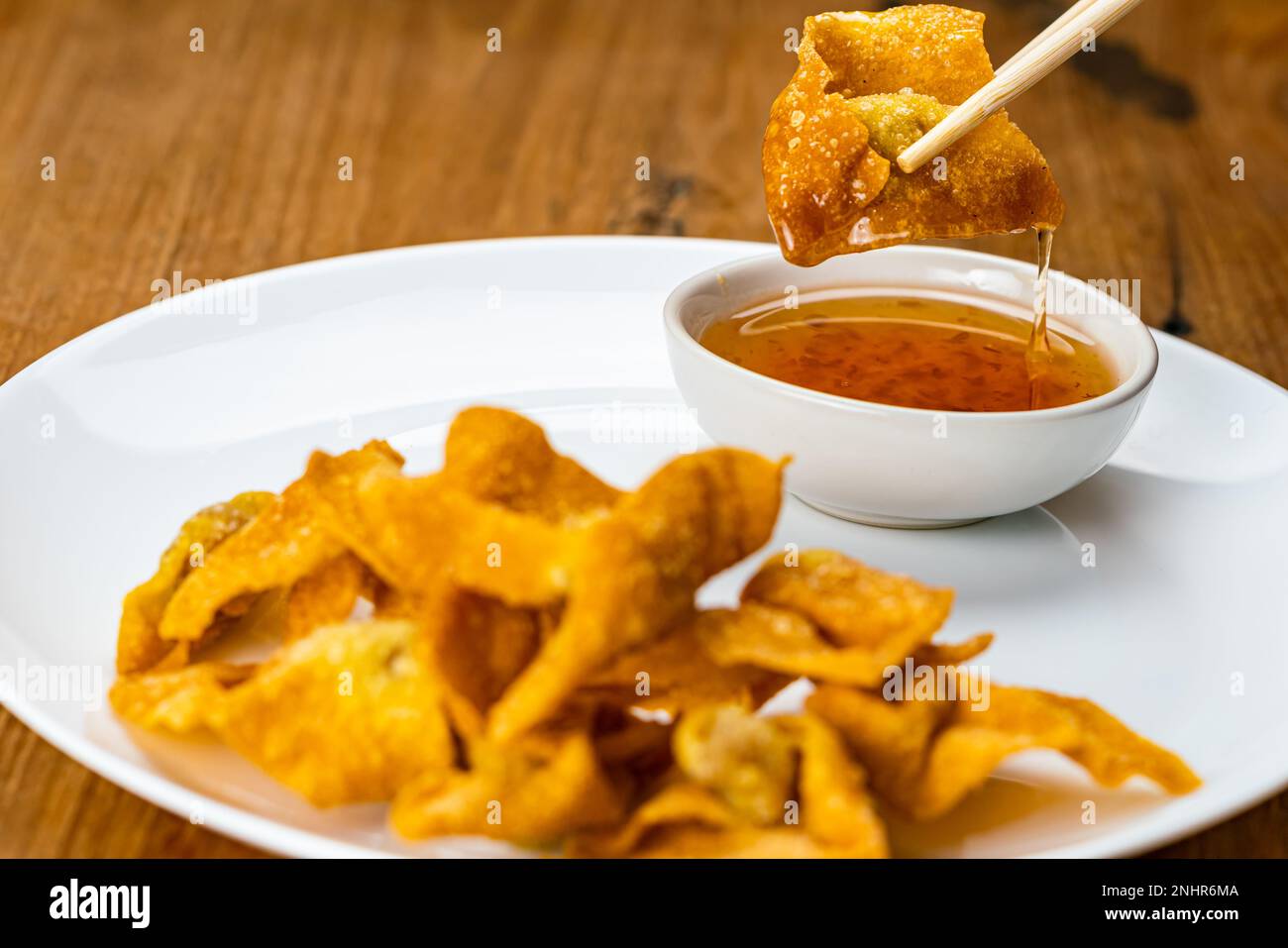 Usando i chopsticks clamp un wonton fritto profondo e croccante squisito fatto in casa in piatto di ceramica bianco che tuffa nella salsa dolce dell'immersione prima del consumo. Foto Stock