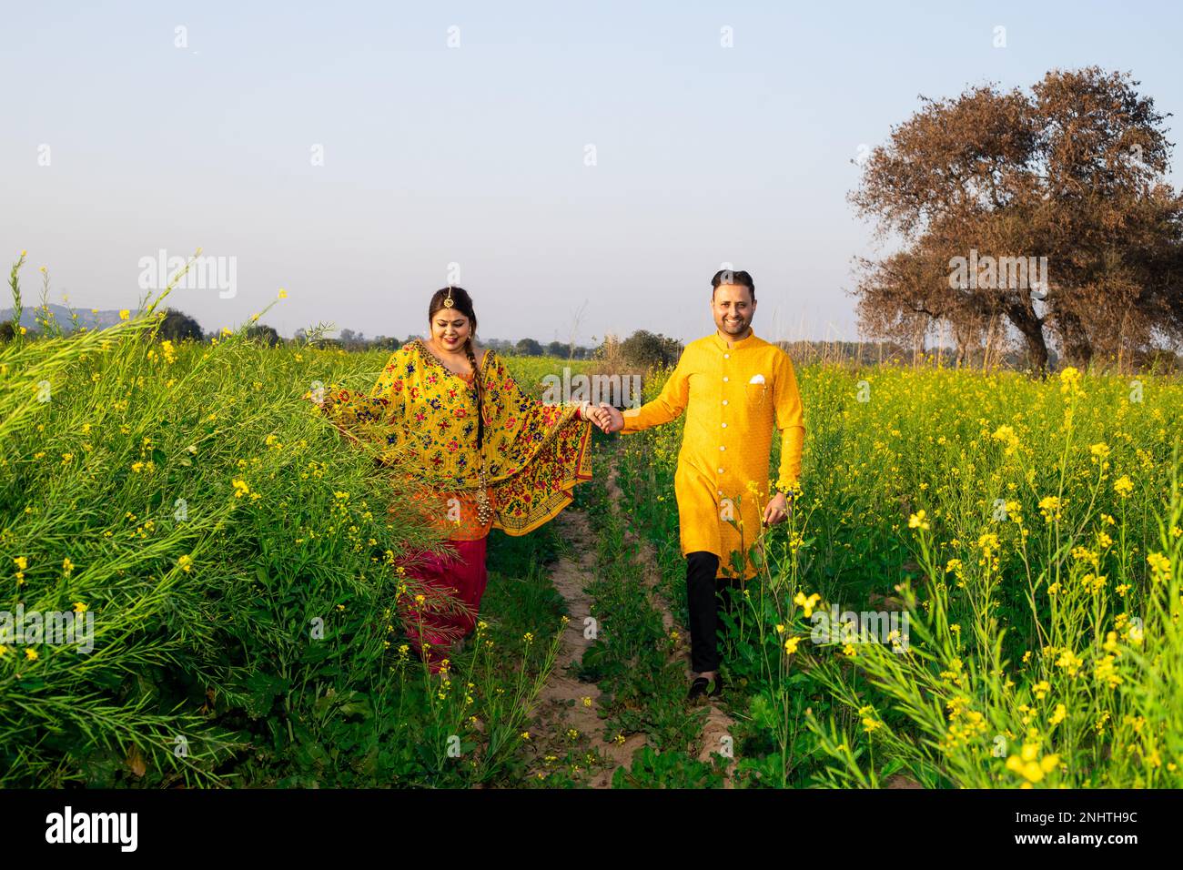 Ritratto di felice giovane coppia indiana punjabi indossare abiti colorati tenendo a vicenda mano camminare insieme in campo agricolo. Foto Stock