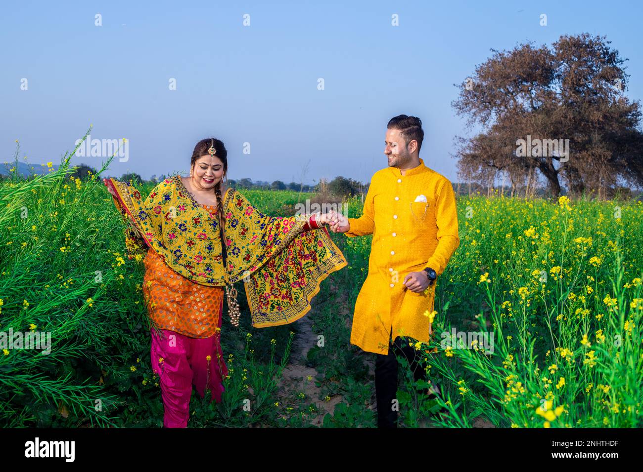 Ritratto di felice giovane coppia indiana punjabi indossare abiti colorati tenendo a vicenda mano camminare insieme in campo agricolo. Foto Stock