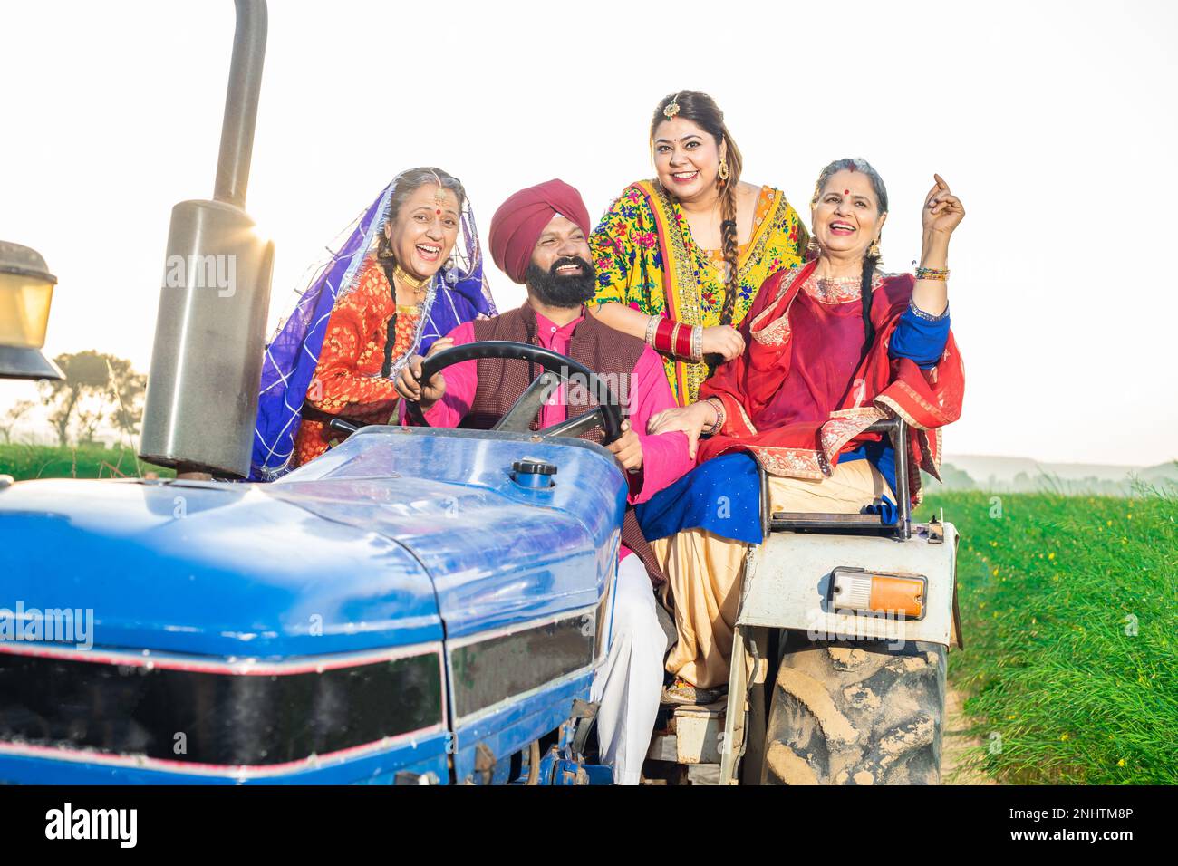 Felice famiglia contadina punjabi sikh seduta sul trattore ballando e festeggiando all'aperto. punjab e haryana, India rurale. Foto Stock