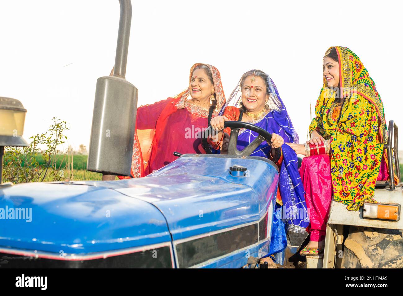 Gruppo di donne punjab felice che guidano il trattore in campo agricolo all'aperto. India rurale. Foto Stock