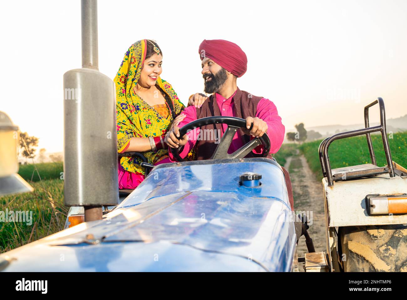 Giovane coppia felice punjab sikh guida trattore in campo agricolo all'aperto. India rurale. Foto Stock