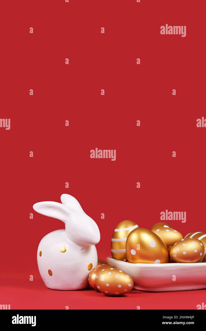 Uova di Pasqua dorate dipinte con strisce e puntini e coniglietto su sfondo rosso con spazio copia Foto Stock
