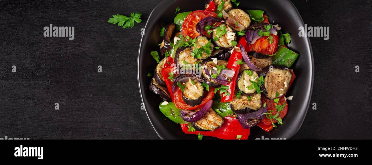 Melanzane alla griglia, peperone, zucchine, cipolla rossa, pomodoro con aglio su un piatto nero. Vista dall'alto, banner Foto Stock