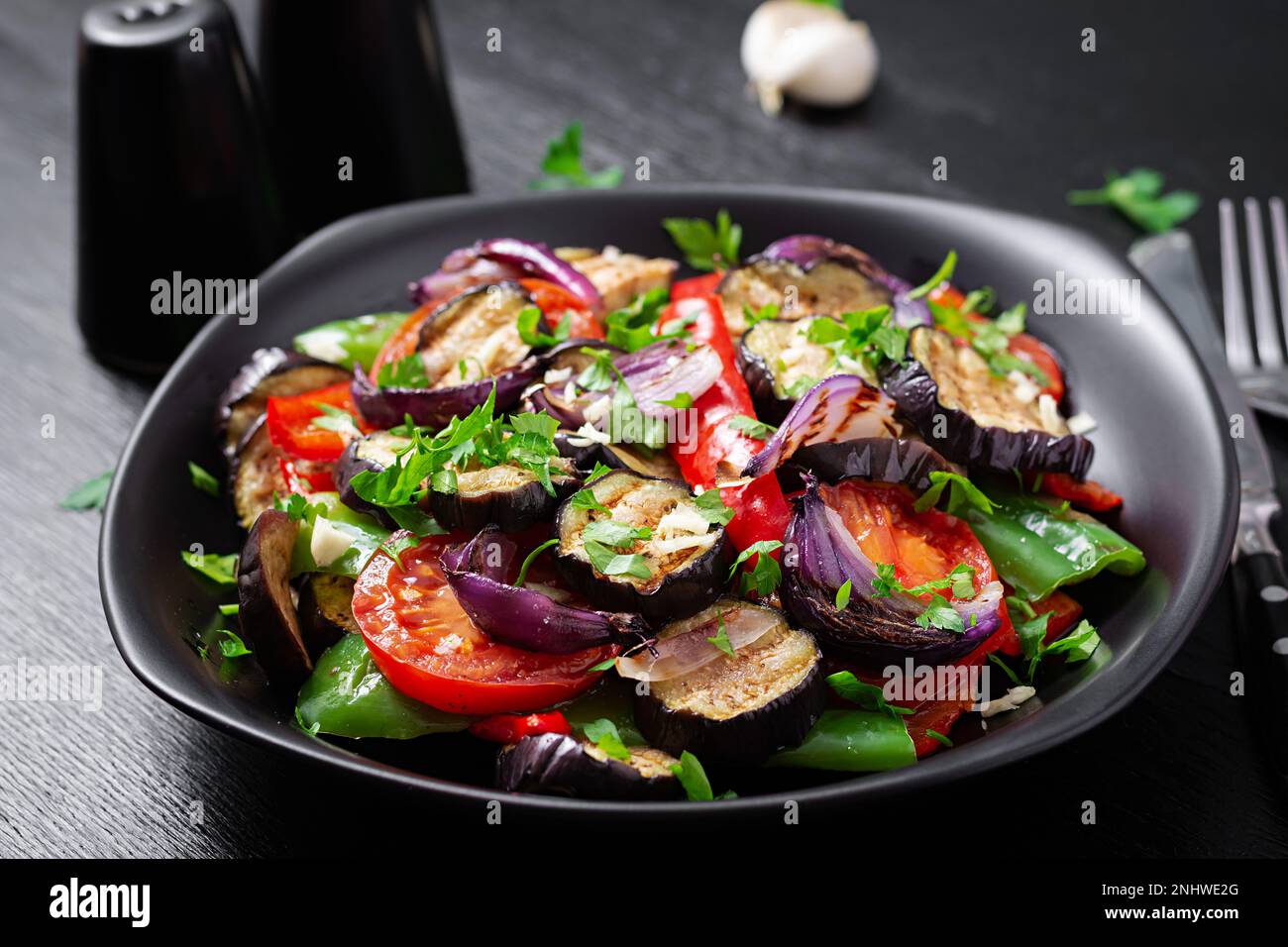 Melanzane alla griglia, peperone, zucchine, cipolla rossa, pomodoro con aglio su un piatto nero. Foto Stock