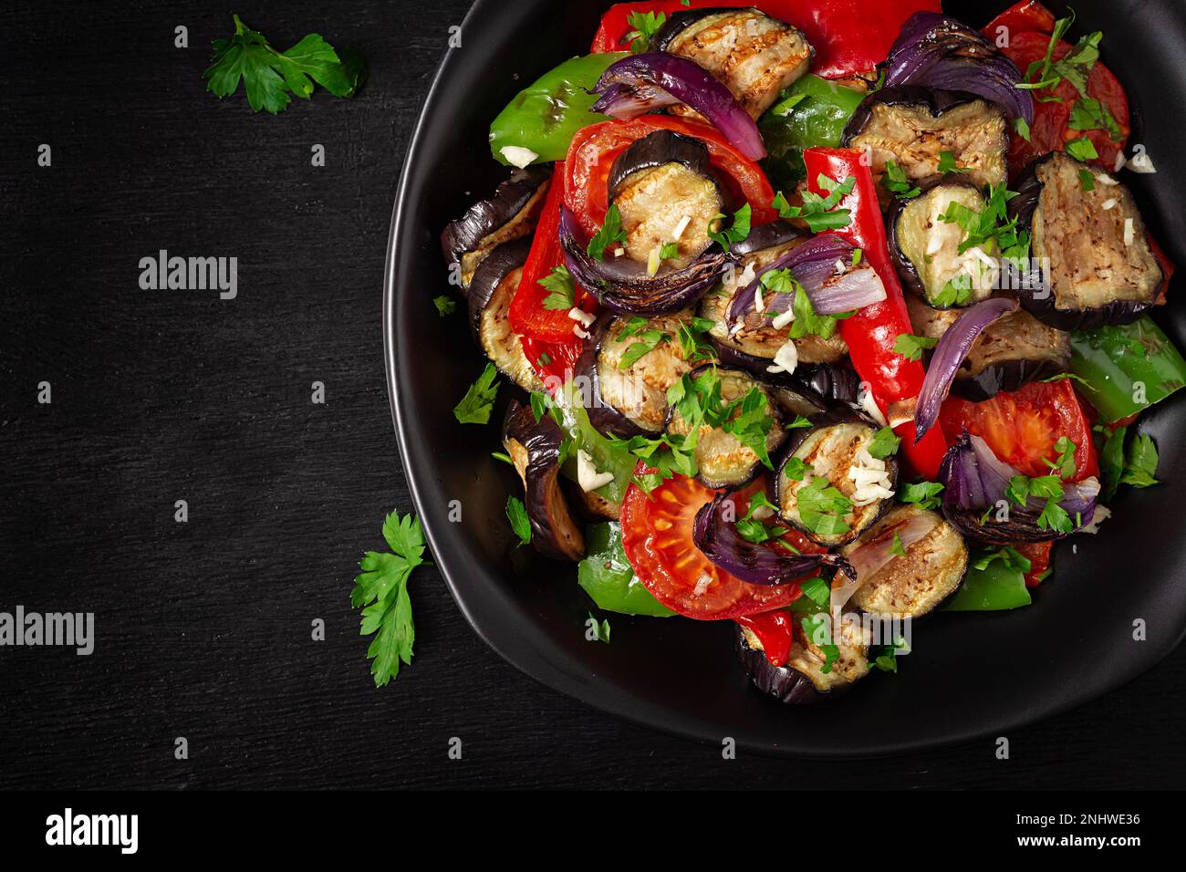 Melanzane alla griglia, peperone, zucchine, cipolla rossa, pomodoro con aglio su un piatto nero. Vista dall'alto, sopra Foto Stock