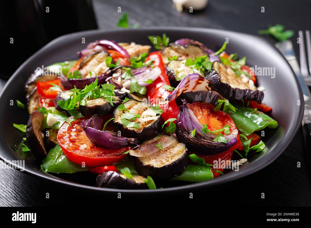 Melanzane alla griglia, peperone, zucchine, cipolla rossa, pomodoro con aglio su un piatto nero. Foto Stock