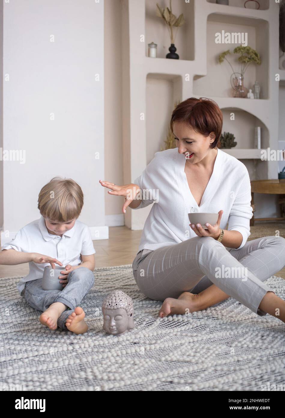 mamma e figlio gioiosi si preparano alla meditazione, giocando insieme seduti sul pavimento a casa. Armonia, tranquillità, benessere, sogni, piacere Foto Stock