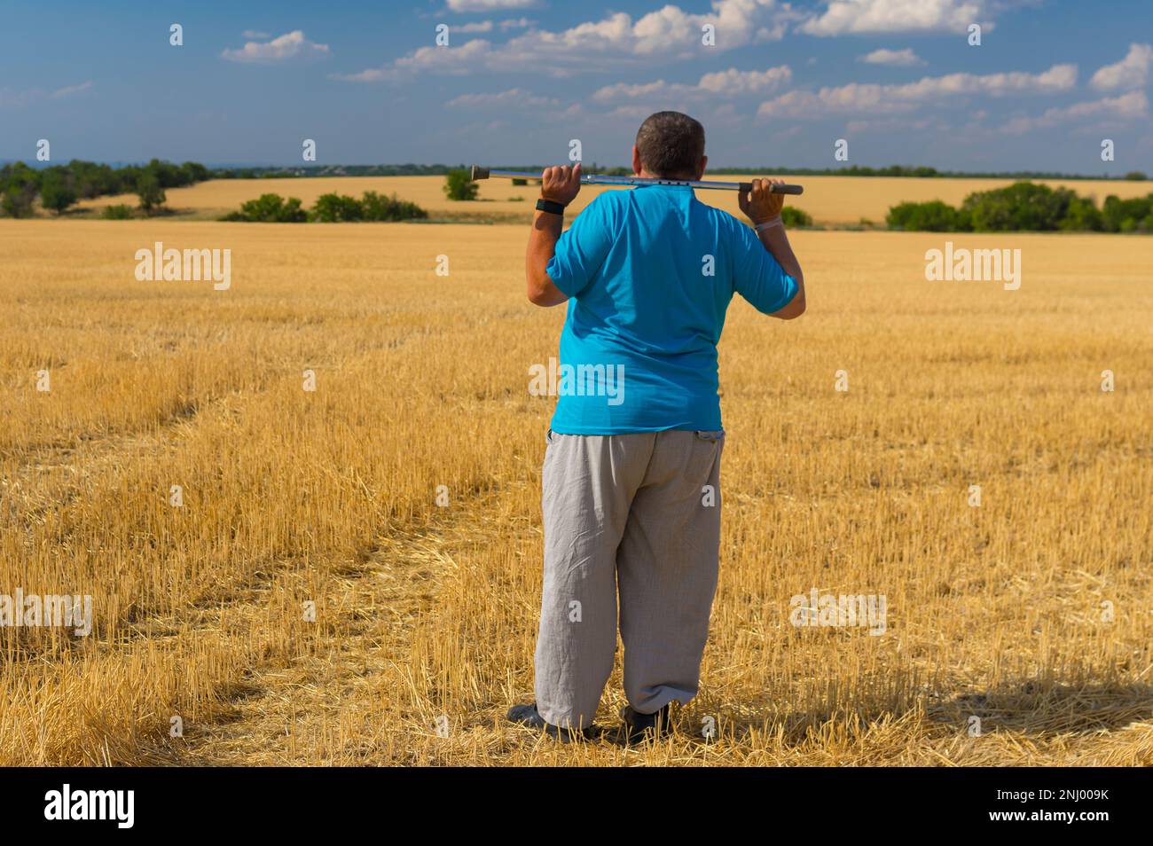 Una grande fama con un palo sul collo in piedi sul campo di grano raccolto in Ucraina e guardarsi intorno Foto Stock
