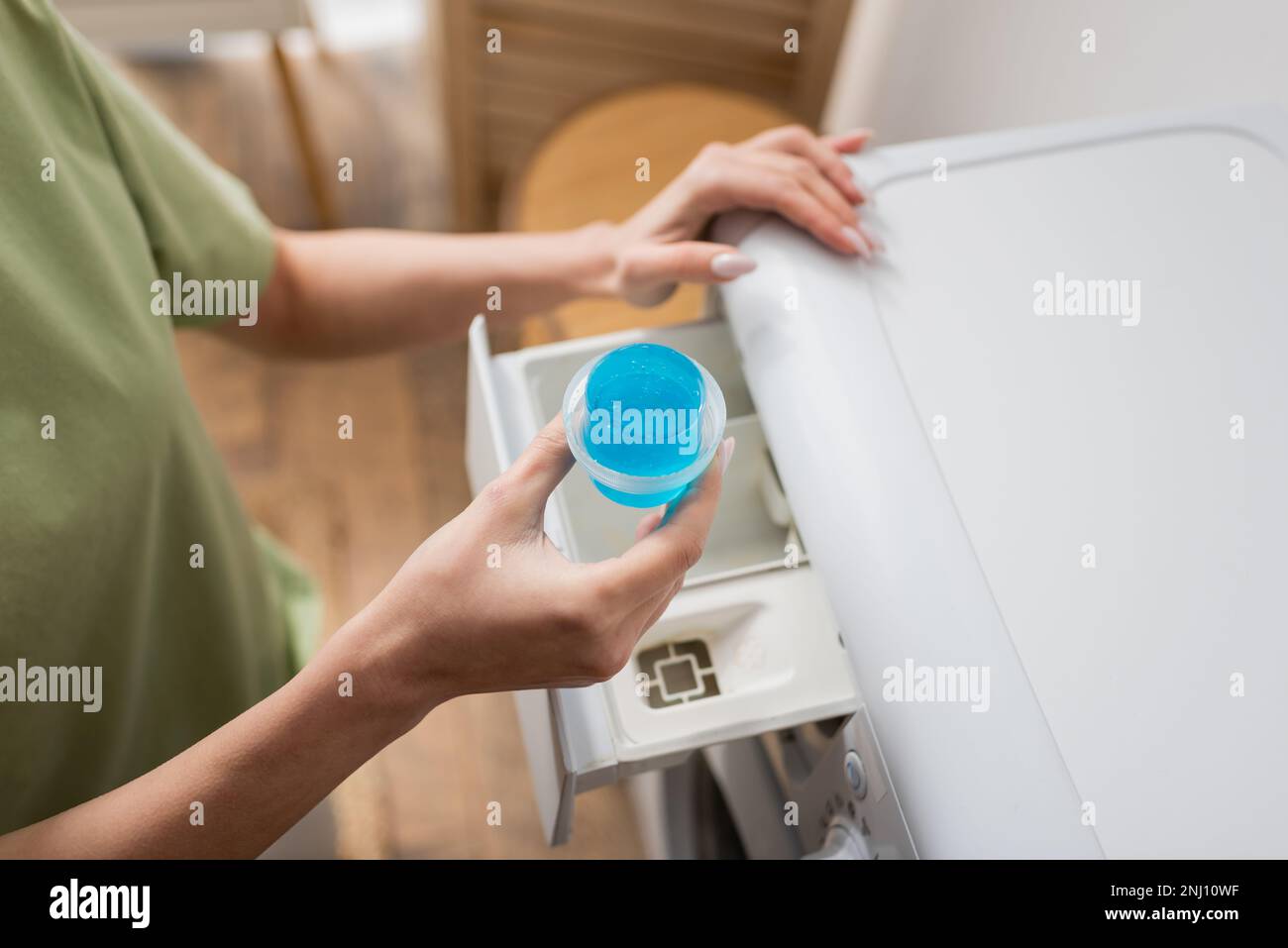 Vista ritagliata della donna che tiene il cappuccio con detergente liquido vicino alla lavatrice, immagine stock Foto Stock