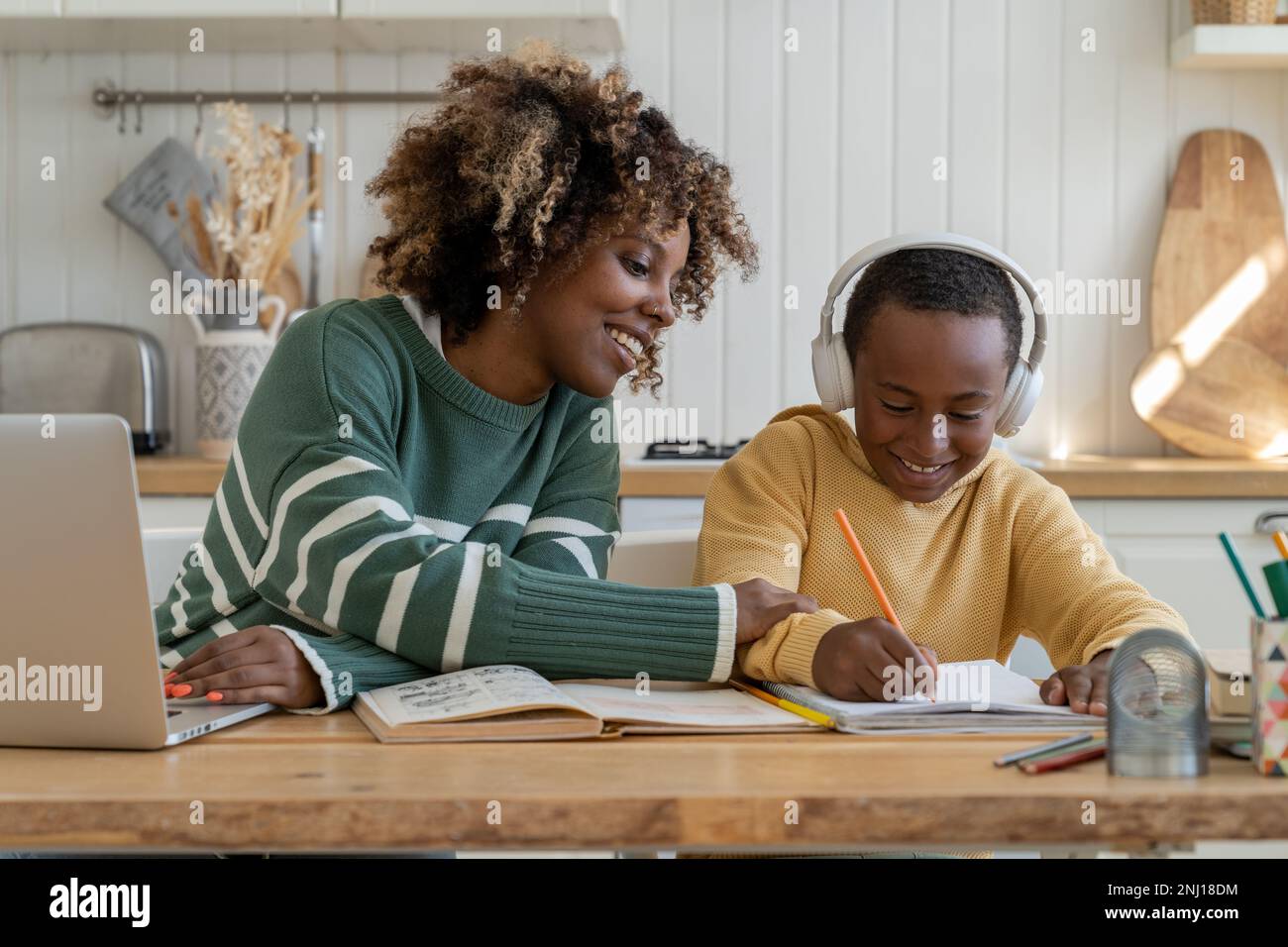Felice ragazzo nero sorridente con madre soddisfatta sedersi alla scrivania con matita scrivere a scuola tutorial Foto Stock