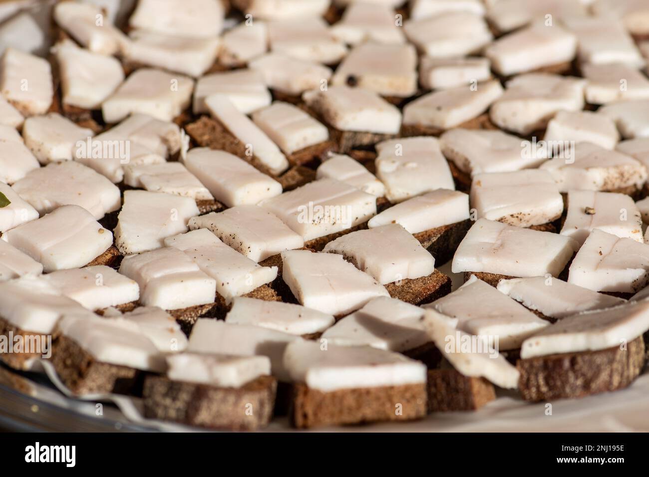 Pezzi di strutto o pancetta, affettati sottilmente per il consumo con pane nero di segale su un tagliere di legno in un mercato di cibo di strada, primo piano Foto Stock