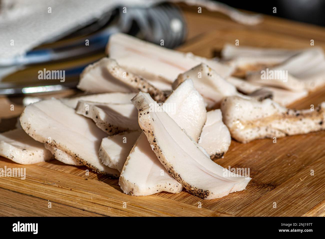 Pezzi di strutto o pancetta, affettati sottilmente per il consumo, su un tagliere di legno in un mercato di cibo di strada, primo piano Foto Stock