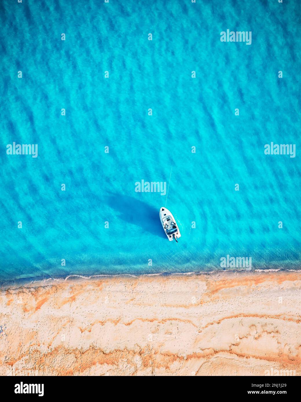 Yacht bianco e onde turchesi dall'alto. Spiaggia con sabbia gialla illuminata dalla luce del sole. Viaggi estate vacanze stagcape sfondo da drone Foto Stock