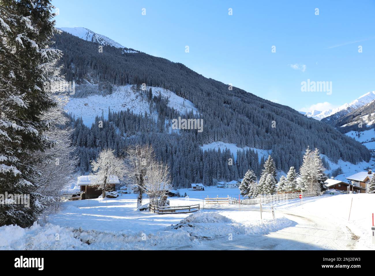 una strada rurale coperta di ghiaccio e alcune case coloniche in una valle di montagna in una bella mattina fredda inverno con neve fresca Foto Stock